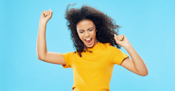 black woman in a yellow shirt, jumping and looking pumped.
